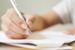 Frau hält Kugelschreiber über ein Blatt Papier